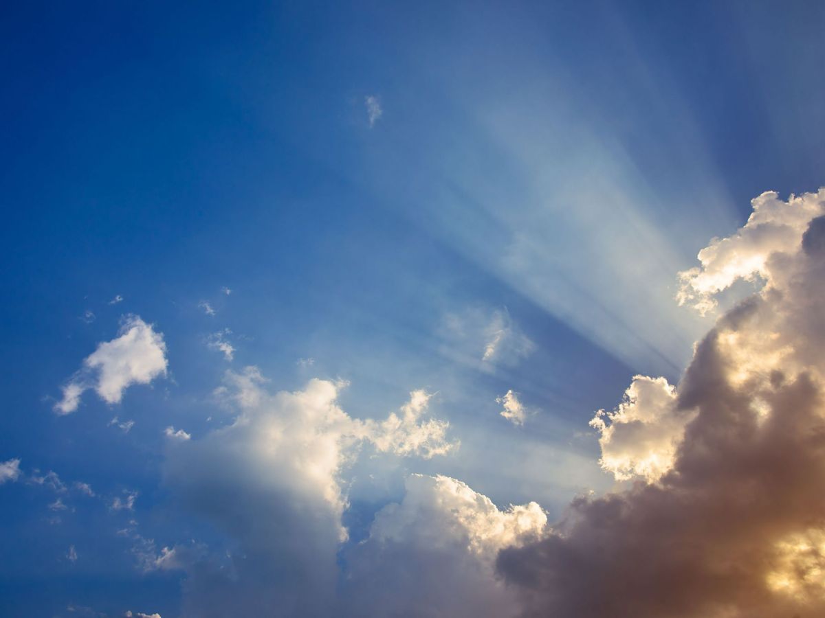 A blue sky with sun rays piercing through clouds