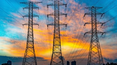 High-voltage transmission towers and power lines silhouetted against an orange sunset sky