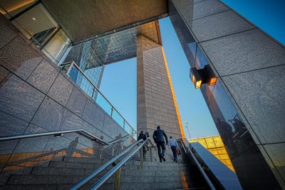 Two businessmen climbing stairs inside a glass office tower, representing incremental steps toward a successful business exit